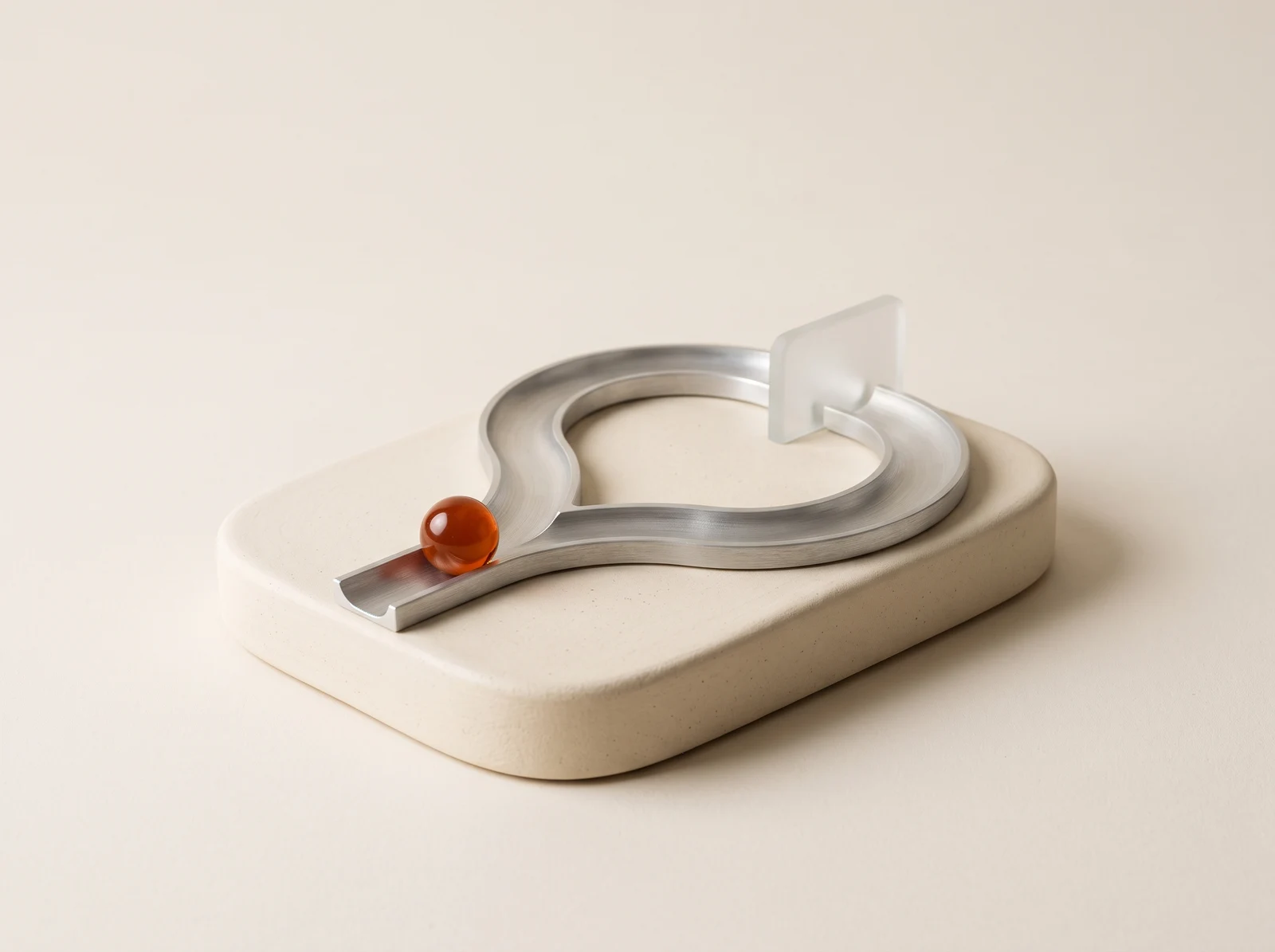 A sculptural metal track with an orange glass bead poised at a fork, on an ivory ceramic base.